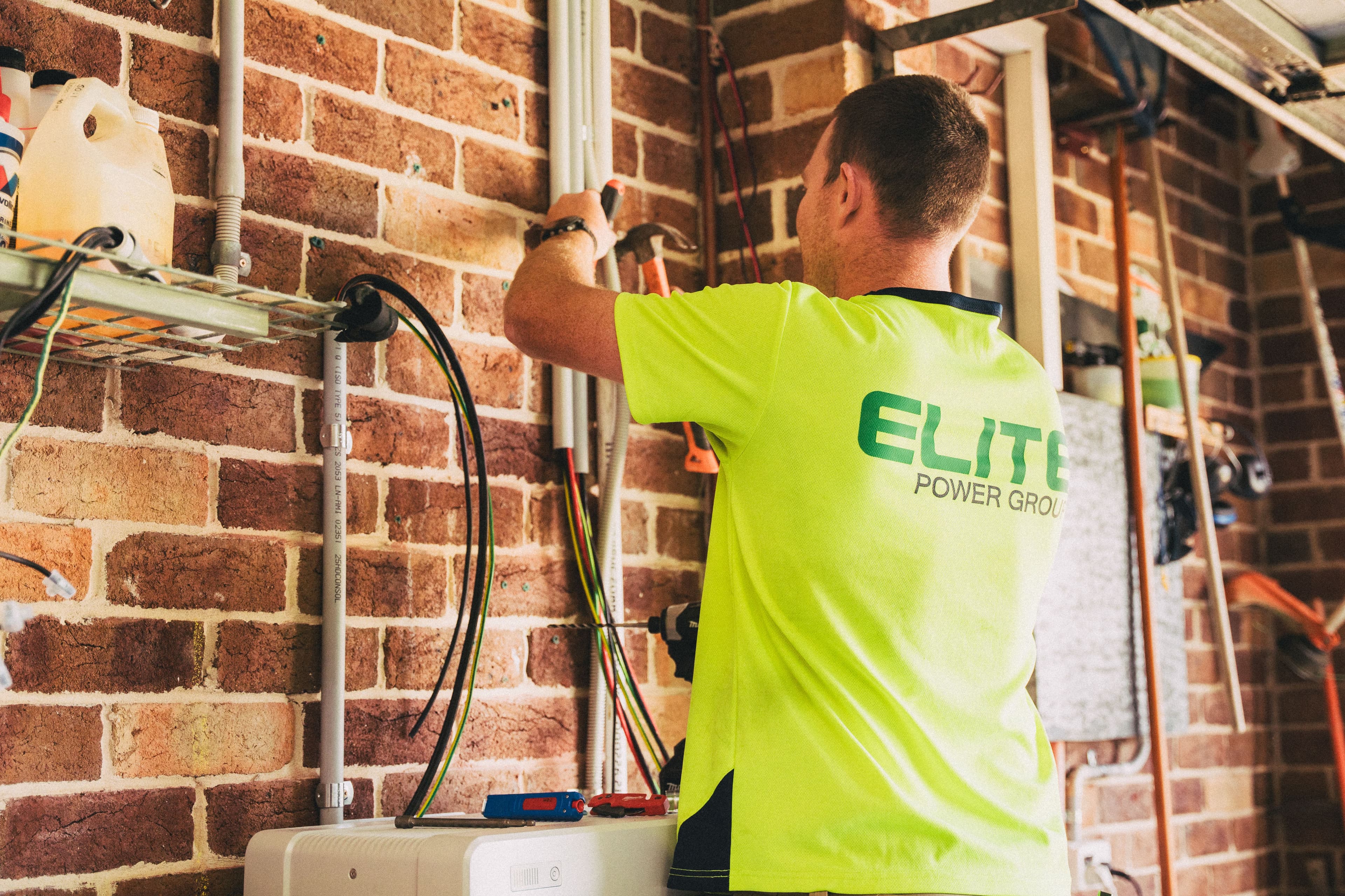 Voltline electrician wiring a panel against a brick wall